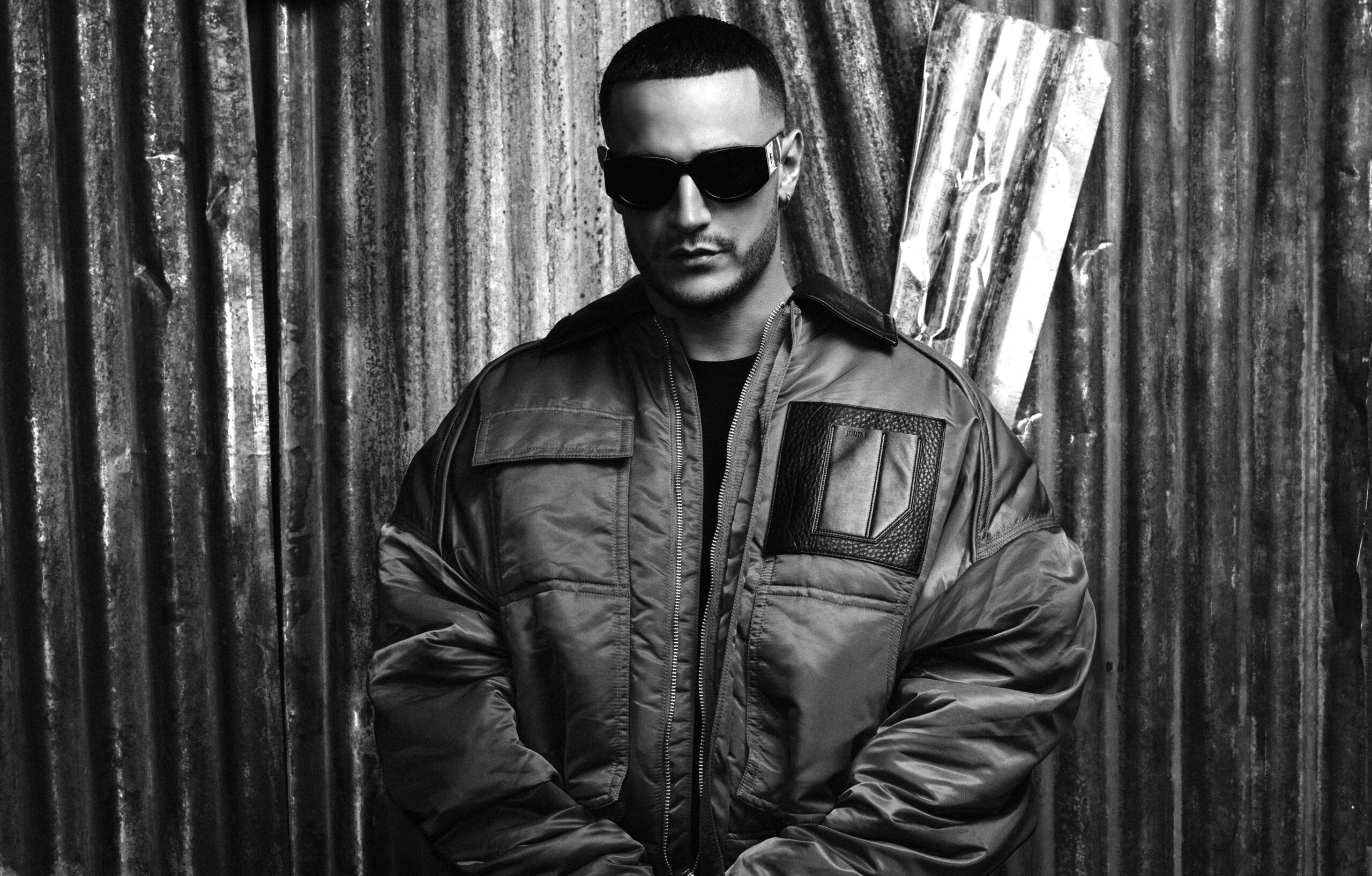 En concert à Paris le 10 mai 2025, l'artiste Dj Snake prend la pose dos à un mur en fer, dans un cliché en noir et blanc.